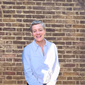 Kate Markey stands in front of a brick wall, smiling at the camera