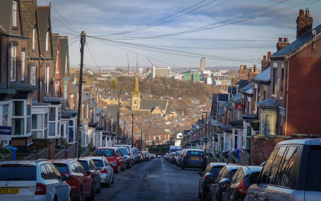 Photo taken looking down from the top of a step road with homes and cars either side of the street