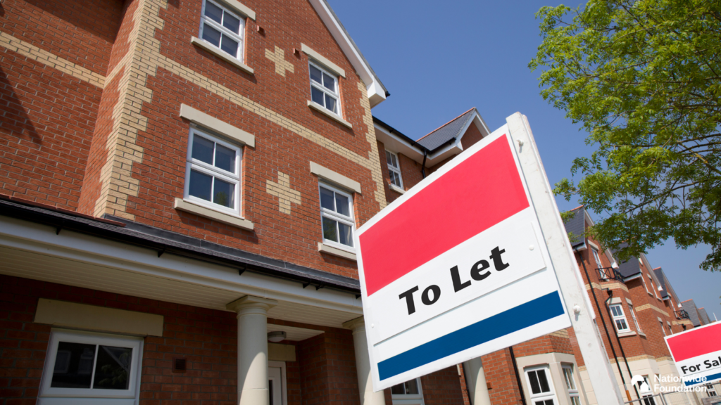 Image shows the front of a red brick house, with four windows and a porch above the entrance below. In front of the house is a sign which reads 'To Let'. To the side of the house is another similar house.