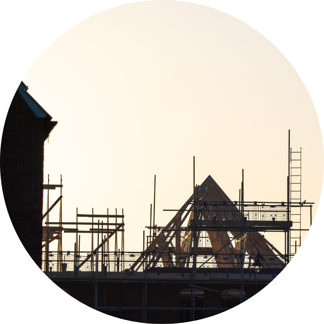 Image shows the roof of a house in a new build house development estate in england - the house is still in construction and the sun is setting behind the house