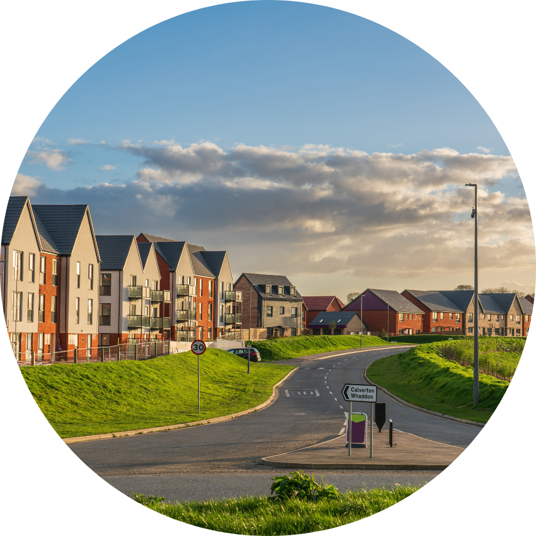 Image shows a new urban housing estate in southern England - the sky is blue with some clouds, and in front of the red brick and white clad houses is vibrant green grass