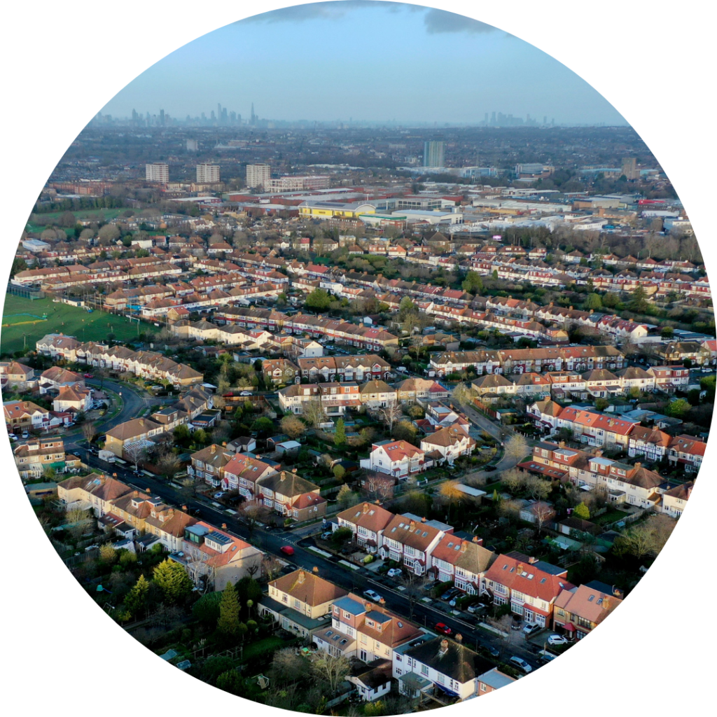 An aerial view of a town or city, above rows of red roofed houses, with an urban town centre in the background