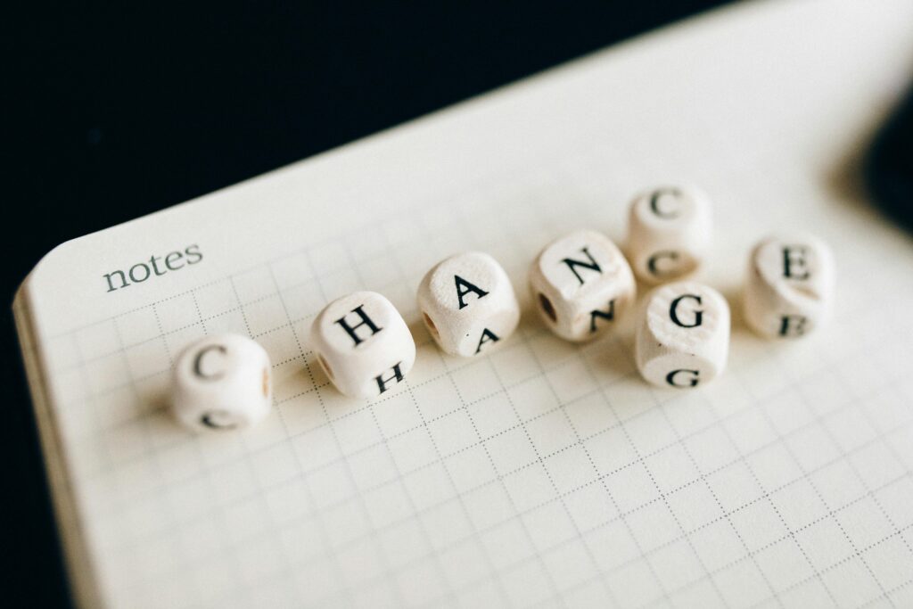 Image shows six dice with letters instead of numbers. The dice sit on top of a square lined book and the letters spell out the word 'change'.