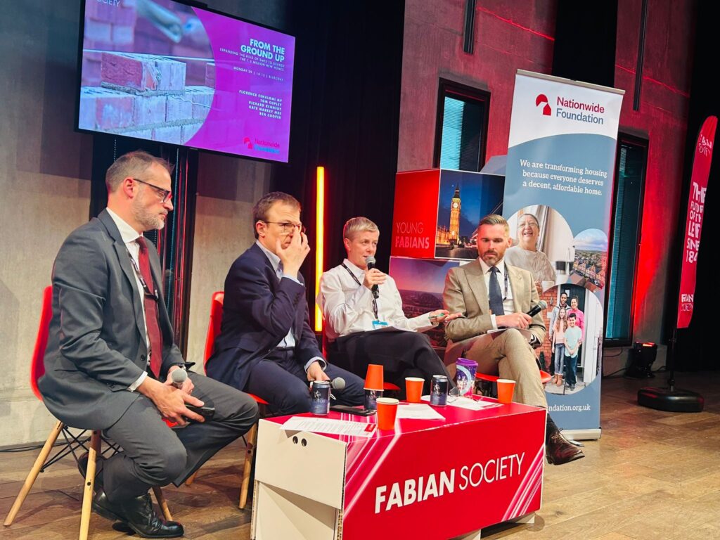 Four people sit behind a table, each with microphones - three men and a woman. The table in front of them says 'Fabian Society'